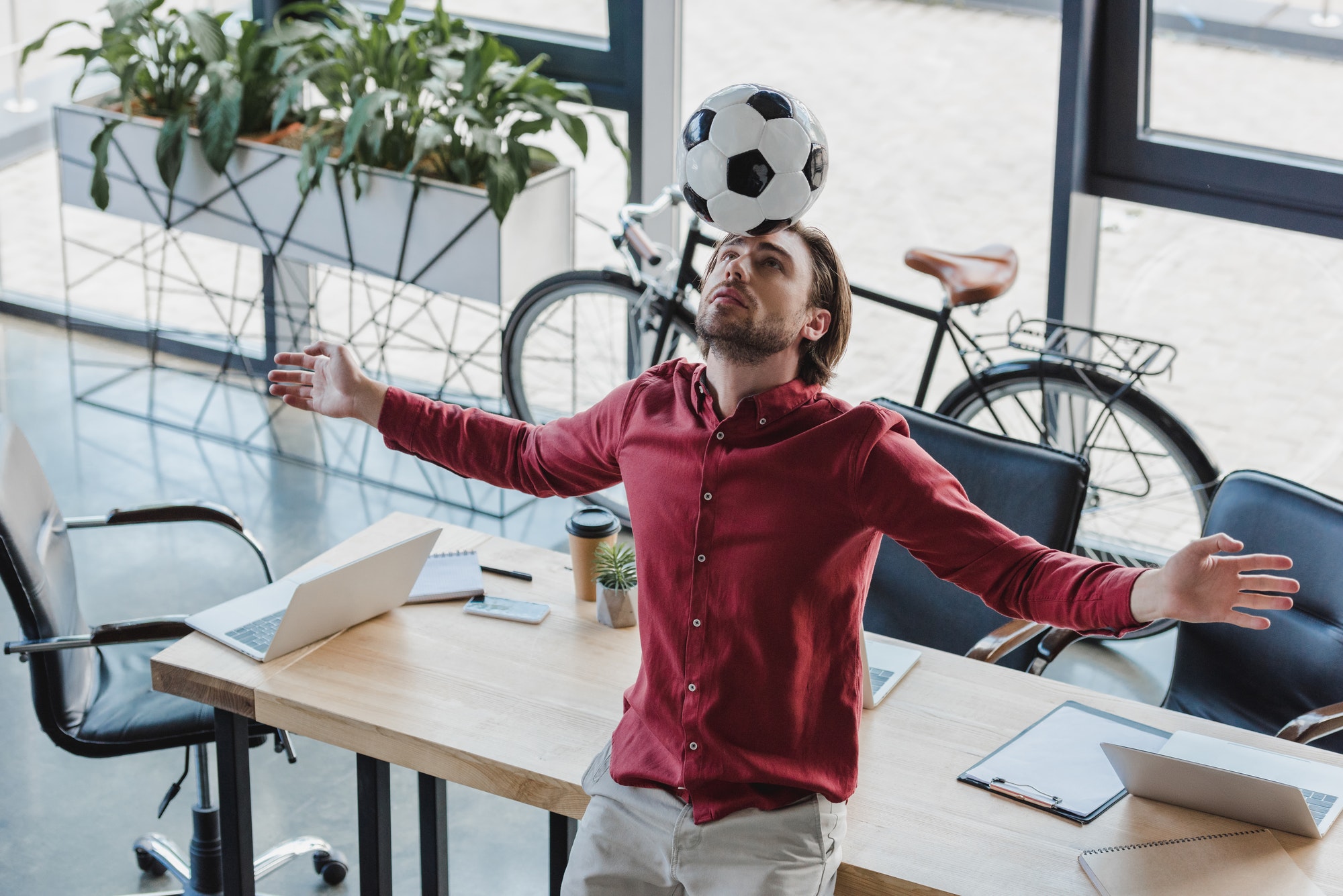 Mann mit ausgestreckten Armen balanciert Ball auf dem Kopf in einem Büro